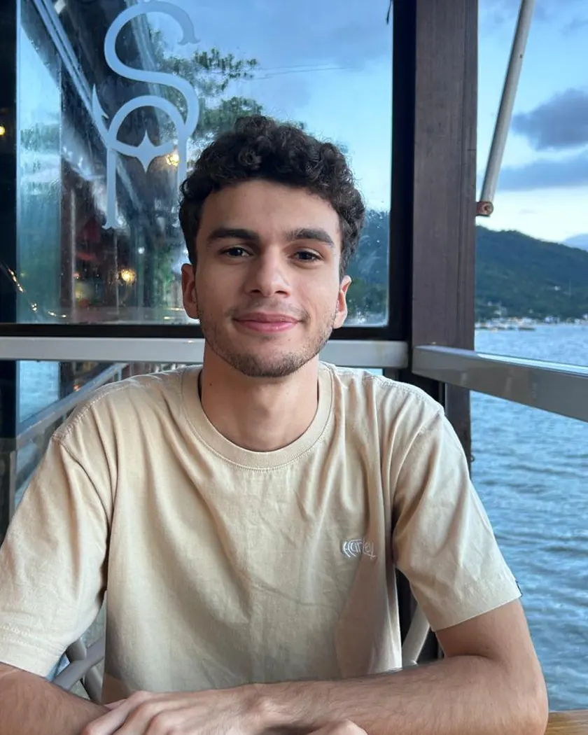 Leonardo Caldeira sentado a uma mesa diante de uma janela, com o mar ao fundo no fim da tarde.