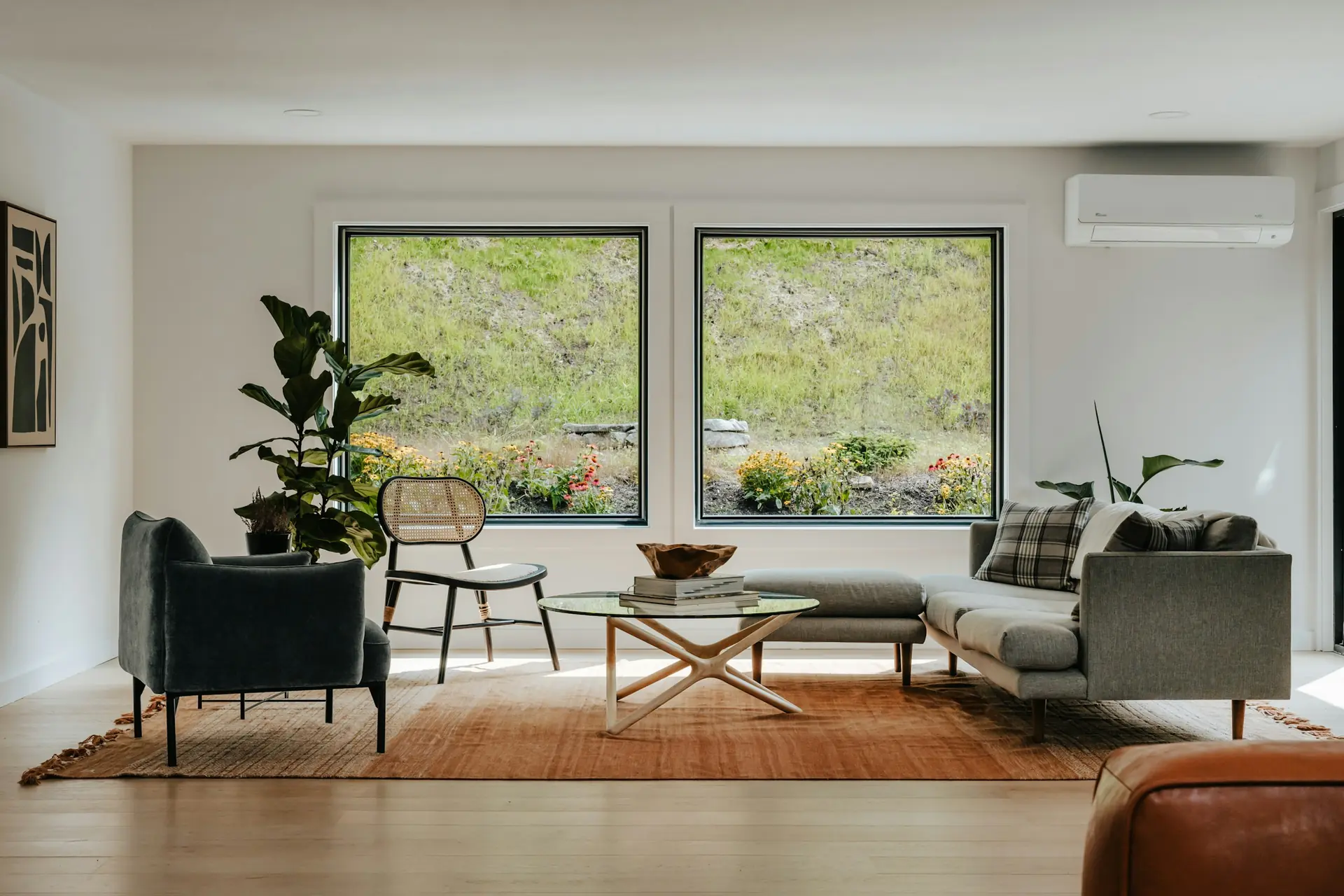 Sala de estar clara, com janelas amplas voltadas para o verde e piso de madeira.